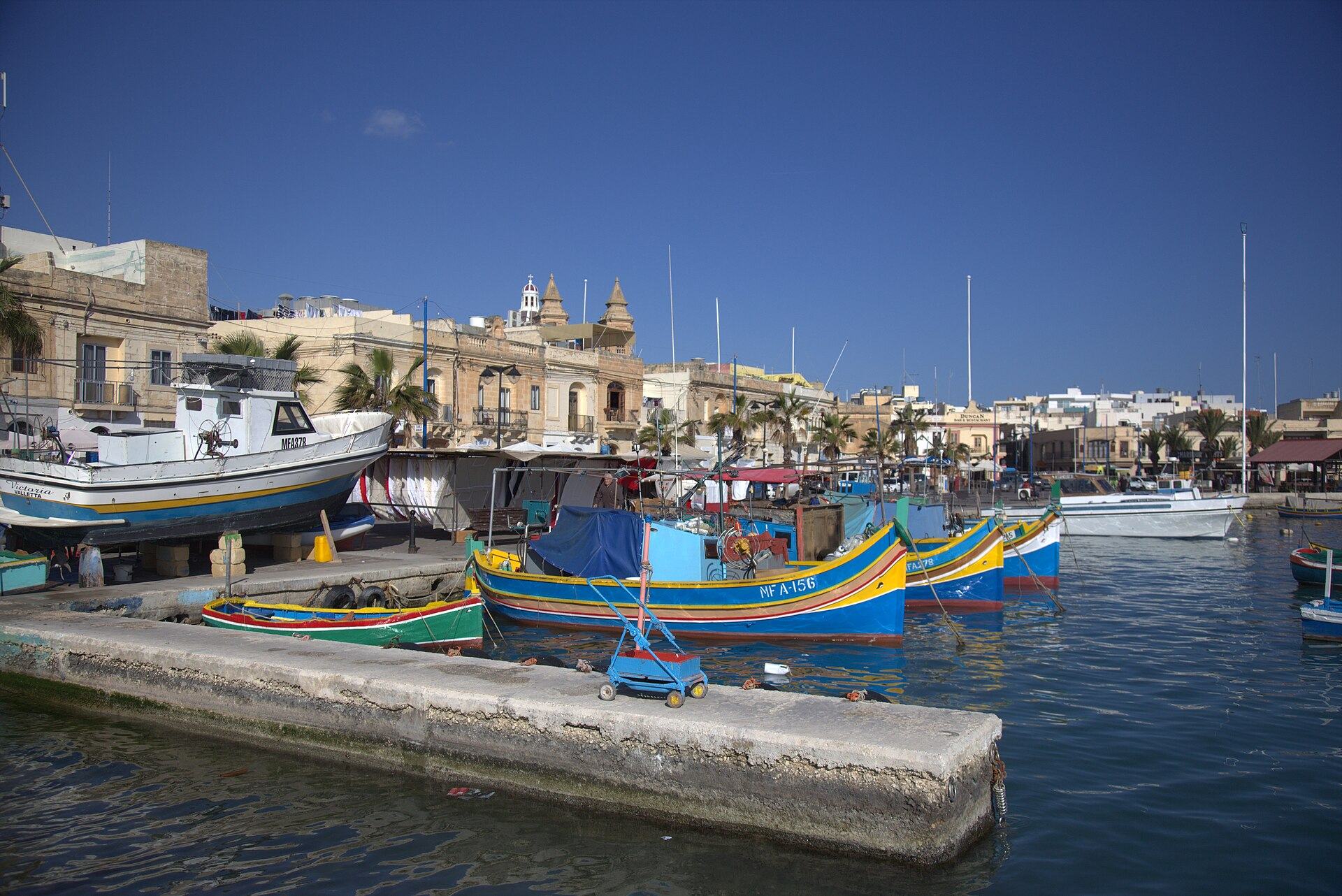 Painted luzzu fishing boats moored along the quay at Marsaxlokk harbour