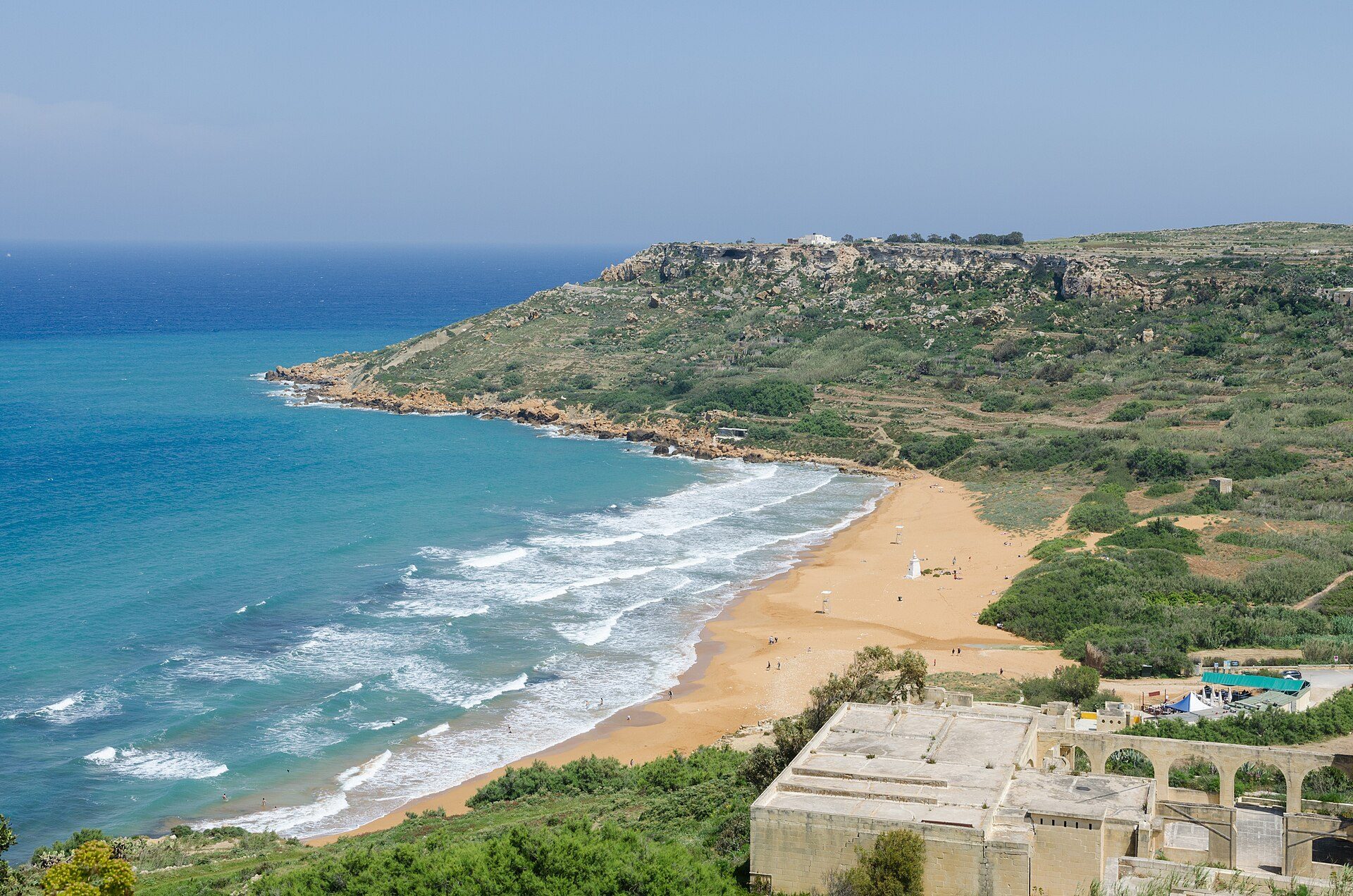 The wide orange-red sand beach at Ramla Bay, Gozo, backed by terraced fields